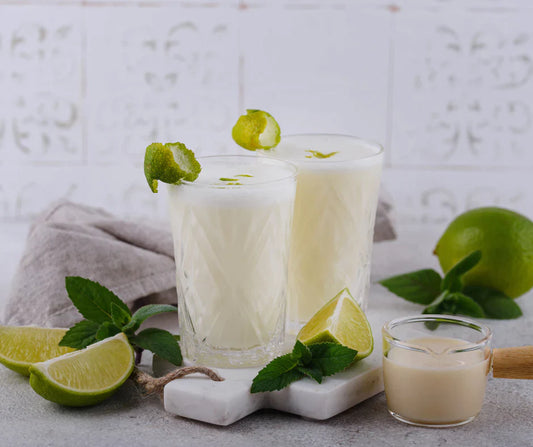 Two pint glasses of Creamy Brazilian Lemonade with mint and wedges of lime.