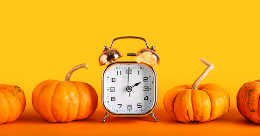 An analog alarm clock with mini tiny orange pumpkins.