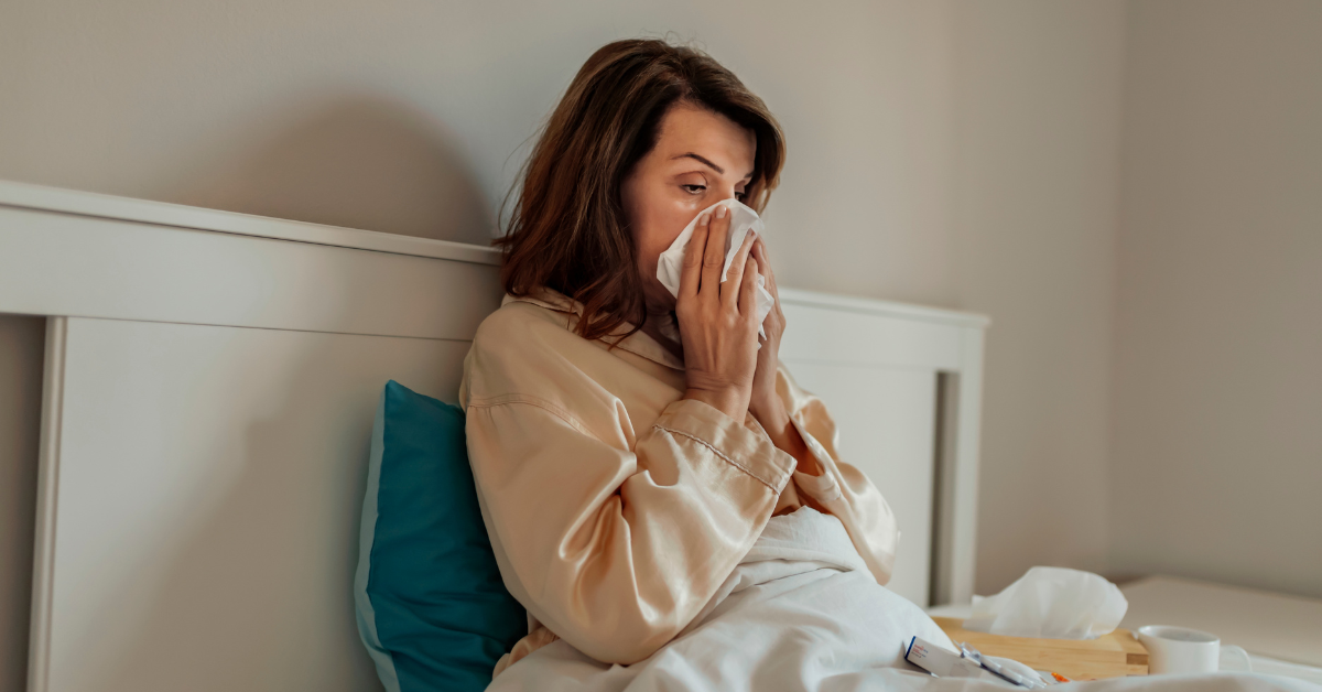 Sick women blowing her nose into a kleenex in bed