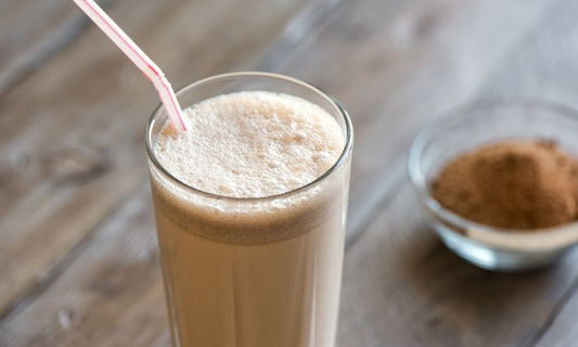 A grass-fed whey protein shake in a tall glass with a straw and a small bowl of whey protein.