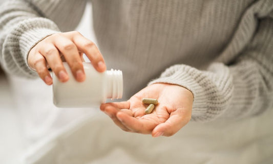 A woman pours supplement pills into her palm from a white bottle. 