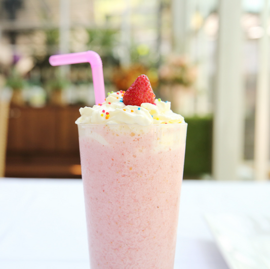 A tall glass of Strawberry Cheesecake Smoothie topped with a strawberry and a straw. 